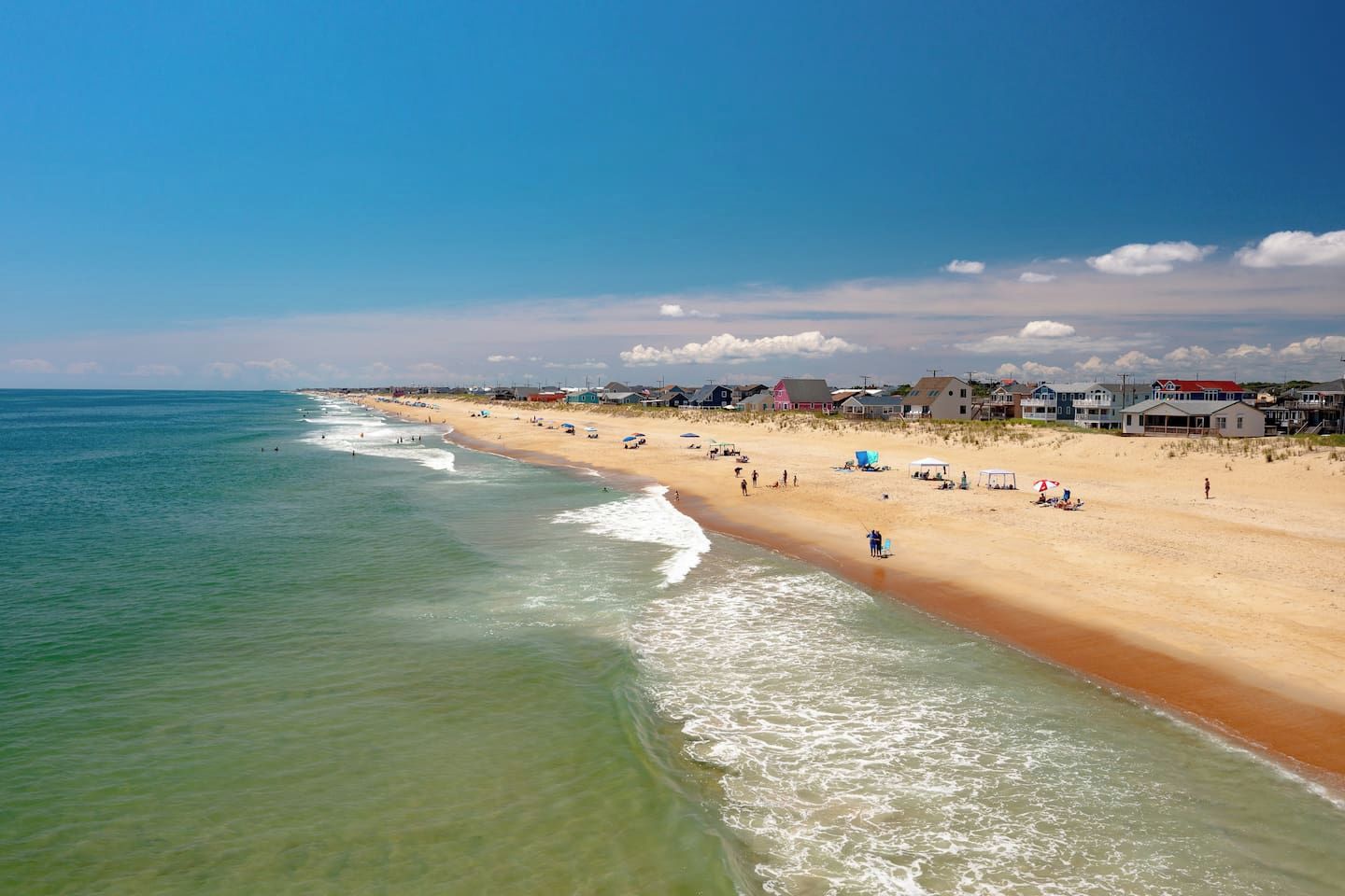 Een strand met helder water, een zandstrand en huizen op de achtergrond.