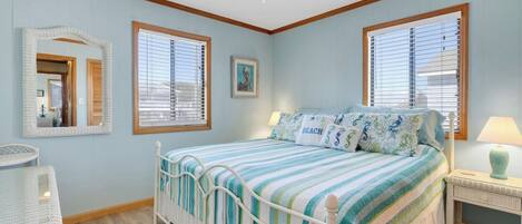 A bedroom with a bed, two windows, a ceiling fan, a bedside table, and a chair.