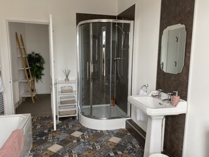 A modern bathroom with a glass shower enclosure, a white sink with a mirror, and patterned floor tiles.