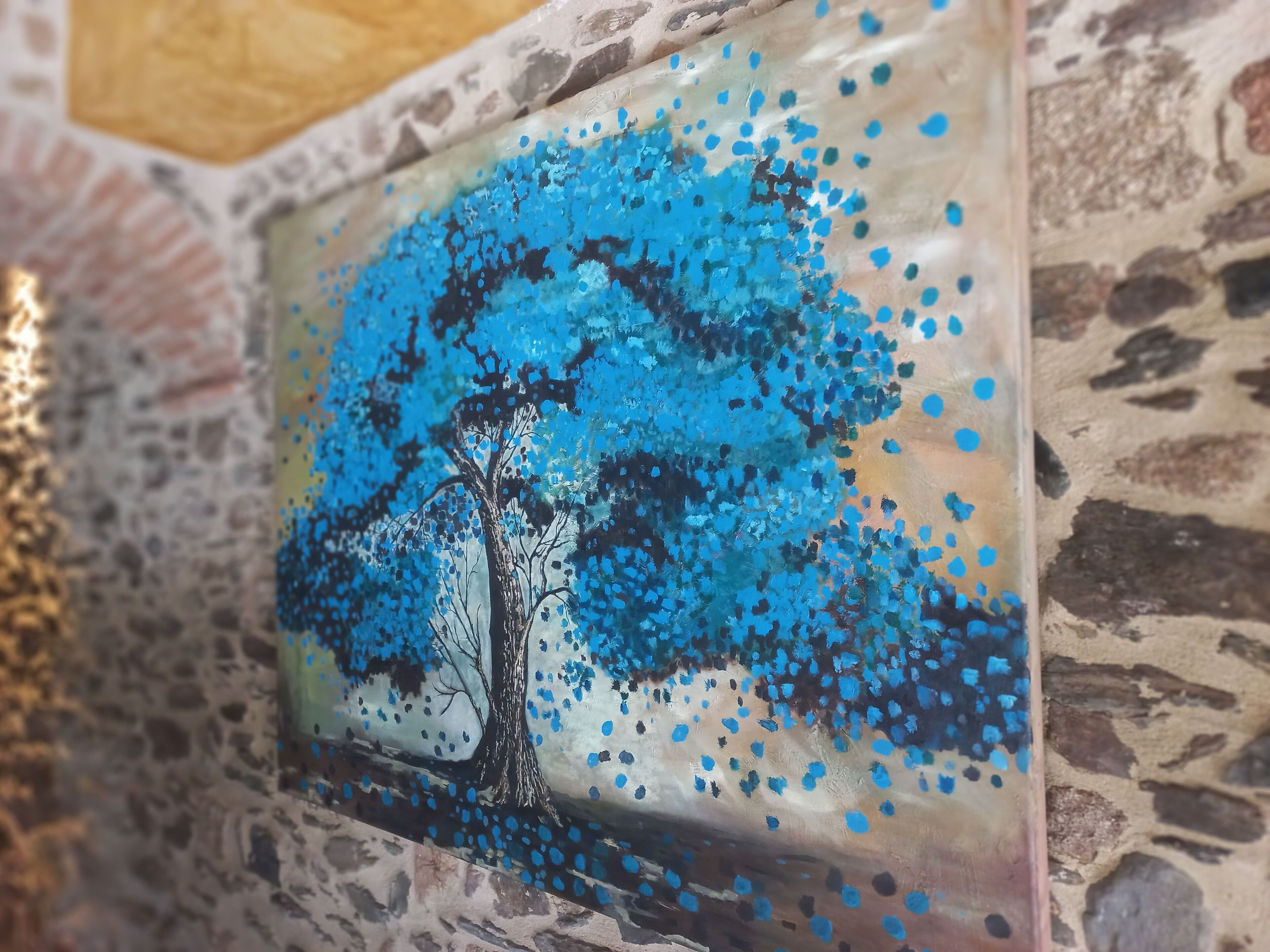 Una pared con un patrón de piedra texturizada y un cuadro enmarcado de un árbol con follaje azul.