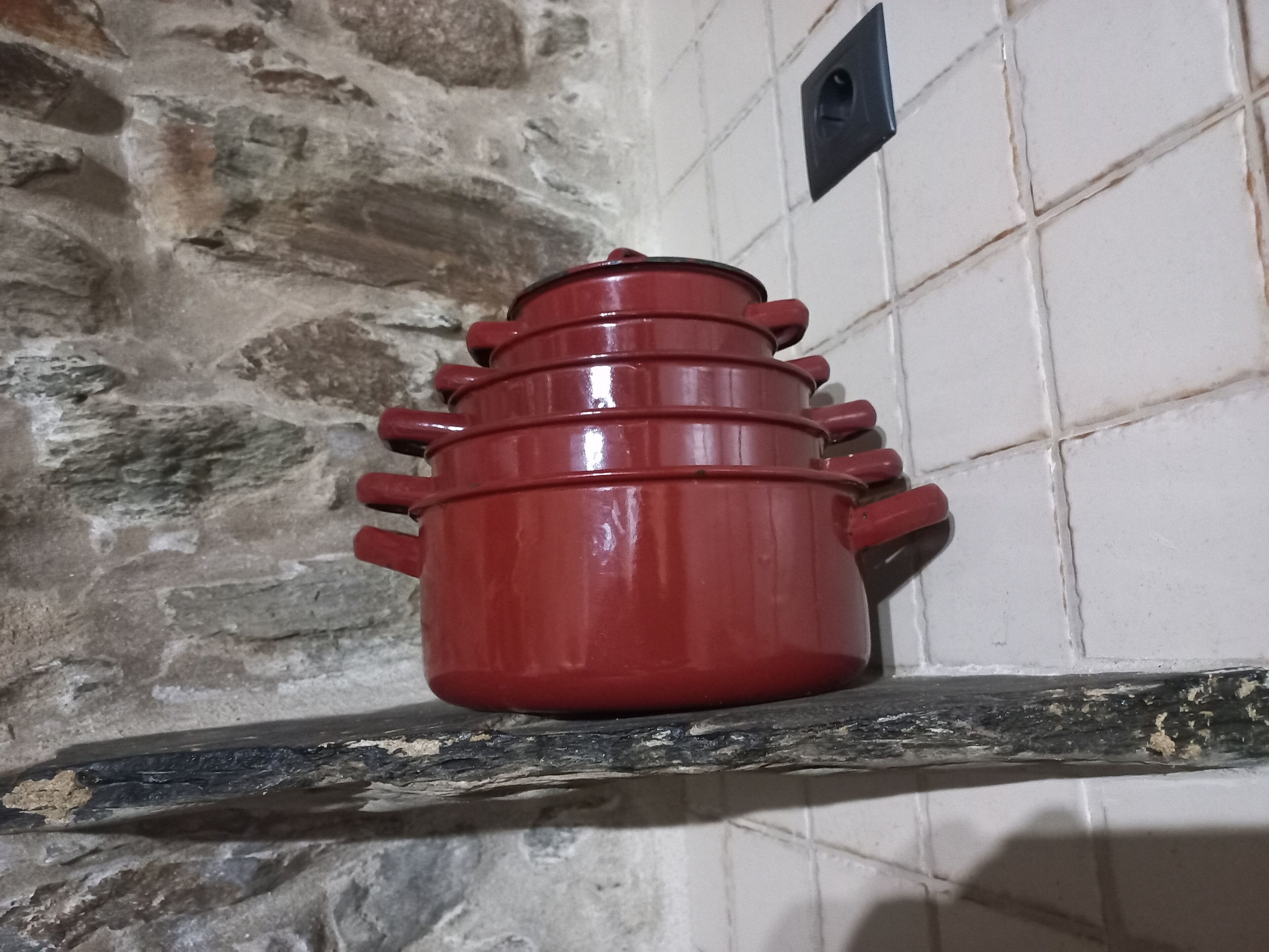 Una olla vermella sobre una prestatgeria, amb un mur de pedra al fons.