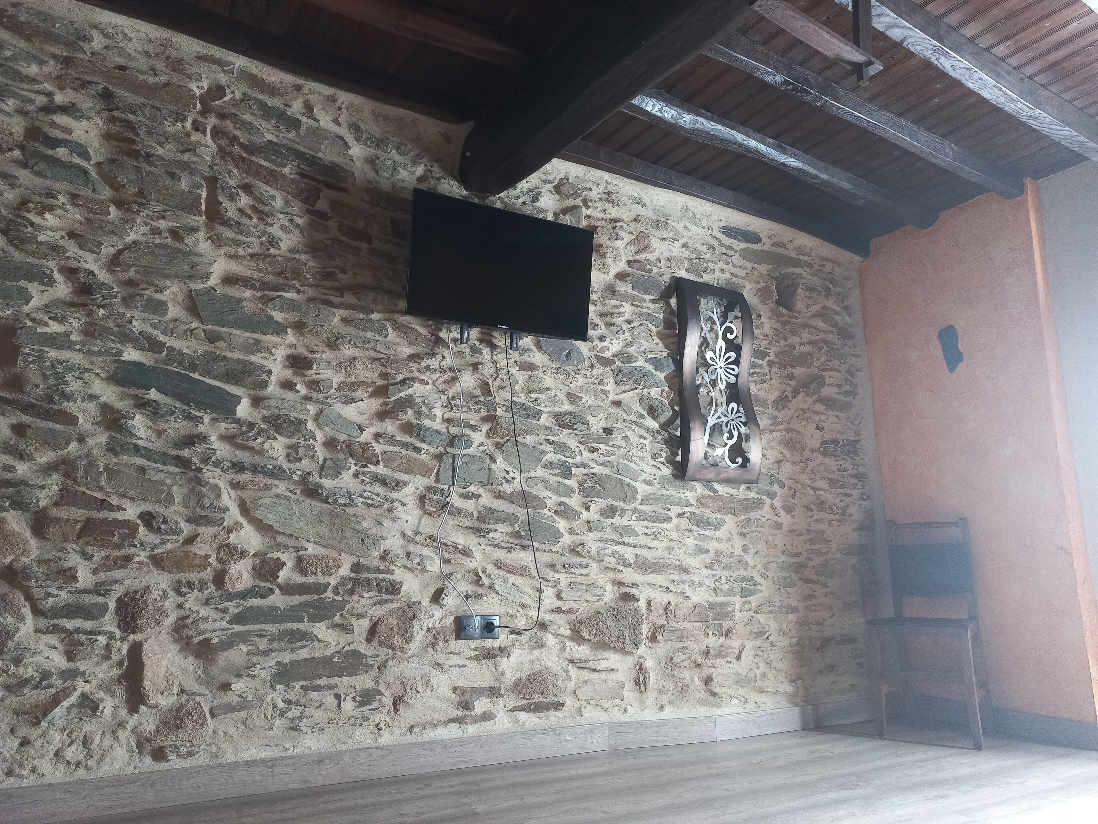 Eine Steinsäule mit einem angebauten Flachbildfernseher, einem dekorativen Metallornament und einem Holzstuhl in der Ecke.