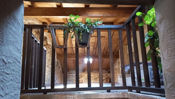Un balcon en bois agrémenté d’une plante suspendue, des murs en pierre et un intérieur rustique.