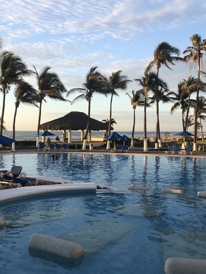 A pool area with lounge chairs, palm trees, and a view of the ocean. - Stunning oceanfront apartment offering breathtaking views (Acapulco de Juárez)