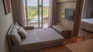 A modern bedroom with a sofa bed, a TV, and a balcony with a view of greenery. - My Mabu (Foz do Iguaçu)