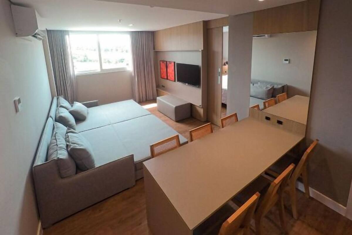 A modern, compact living space with a sofa, a TV, a small dining area, and a window with curtains.