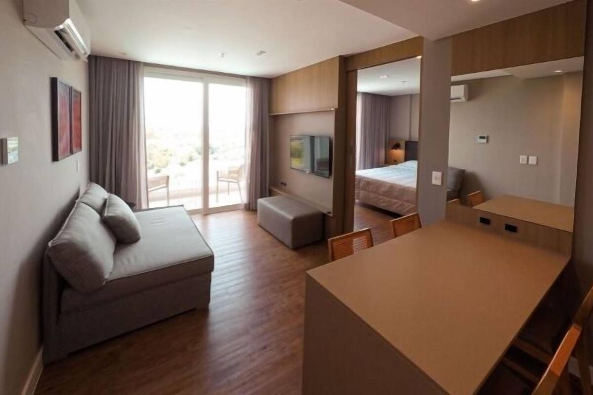 A modern hotel room with a sofa, a small table, a bed, and a large mirror.