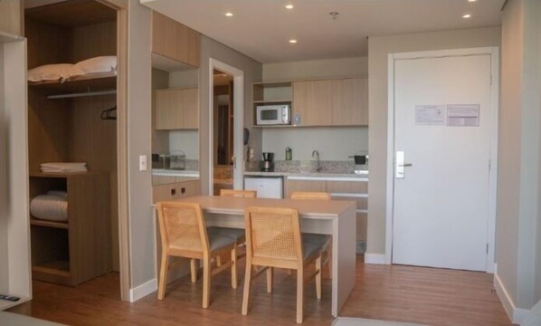 A compact kitchen with a microwave, a coffee maker, and a sink. There is a dining table with two chairs.