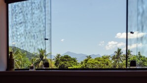 Une vue à travers une fenêtre donnant sur un paysage tropical, avec des palmiers et des montagnes.