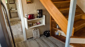 Une cuisine avec un escalier en bois, une machine à café et un grille-pain posés sur une étagère.