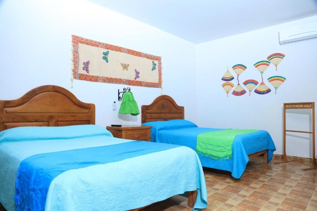 A room with two beds, a green towel on one bed, a wall decoration with butterflies, and a sign on the wall.