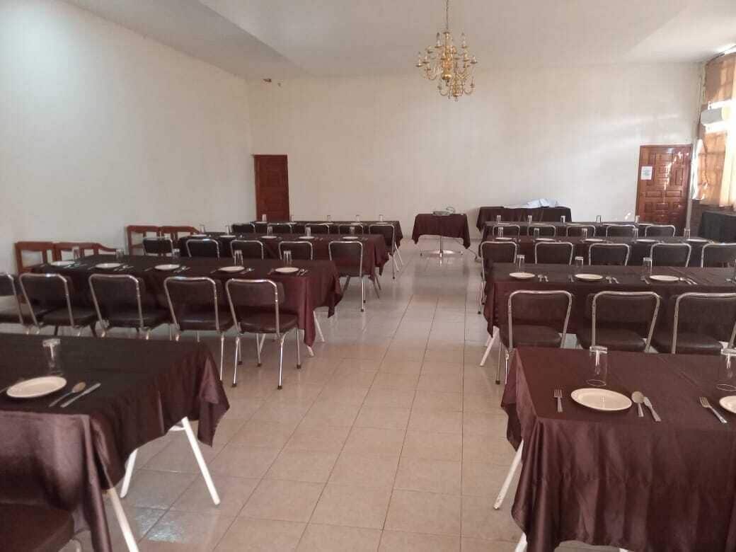 Une salle de conférence avec des rangées de tables et de chaises, un lustre et une porte au fond.