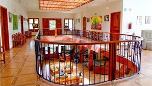 Um interior espaçoso com área central aberta, rodeada por assentos, escadas e teto de madeira.