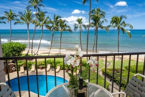 A balcony with a view of the ocean and palm trees, a pool, and a table with a bottle and glasses.