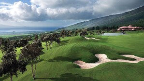 Un campo de golf con un club de campo, árboles y un lago al fondo.