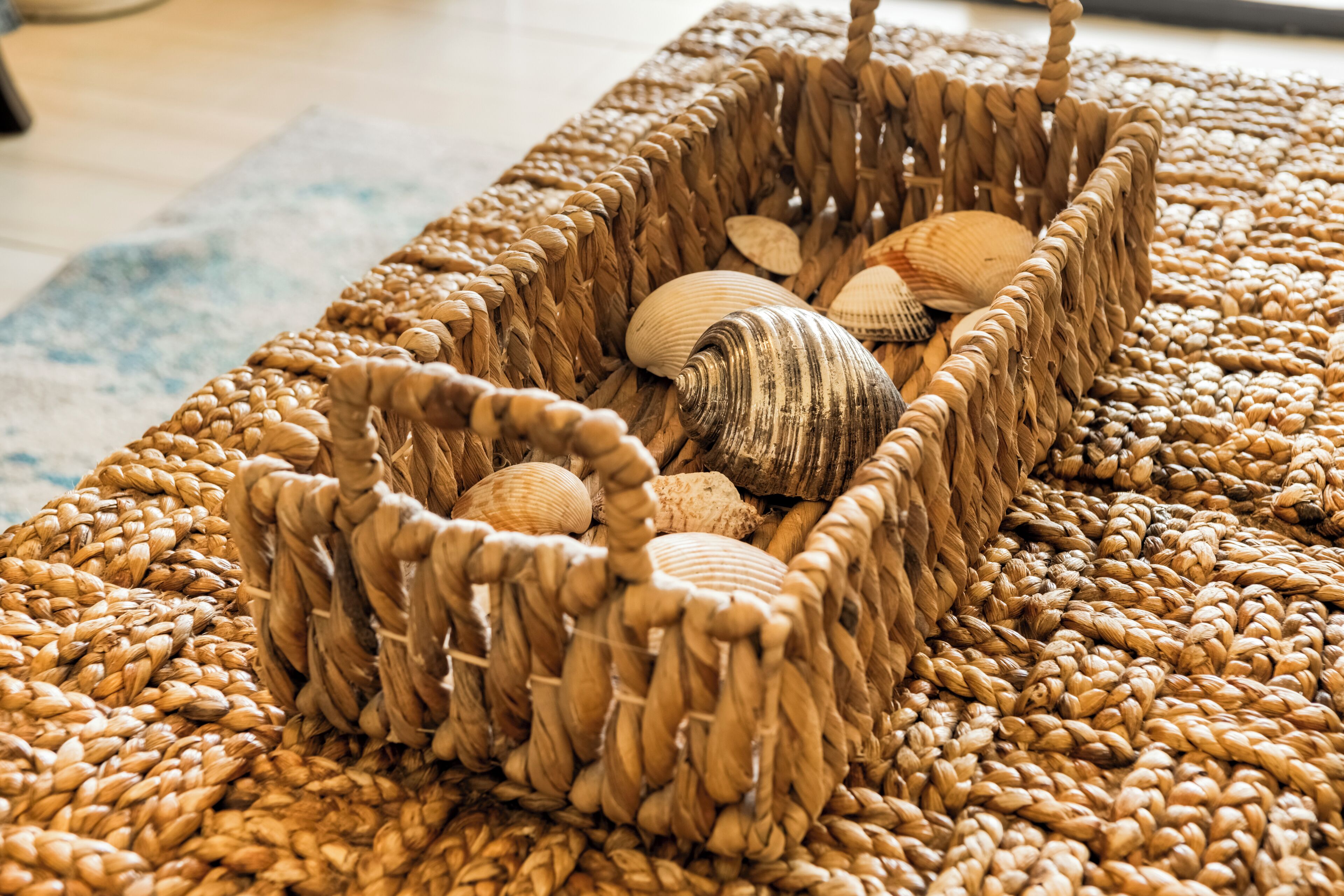 A woven basket filled with seashells on a textured rug.