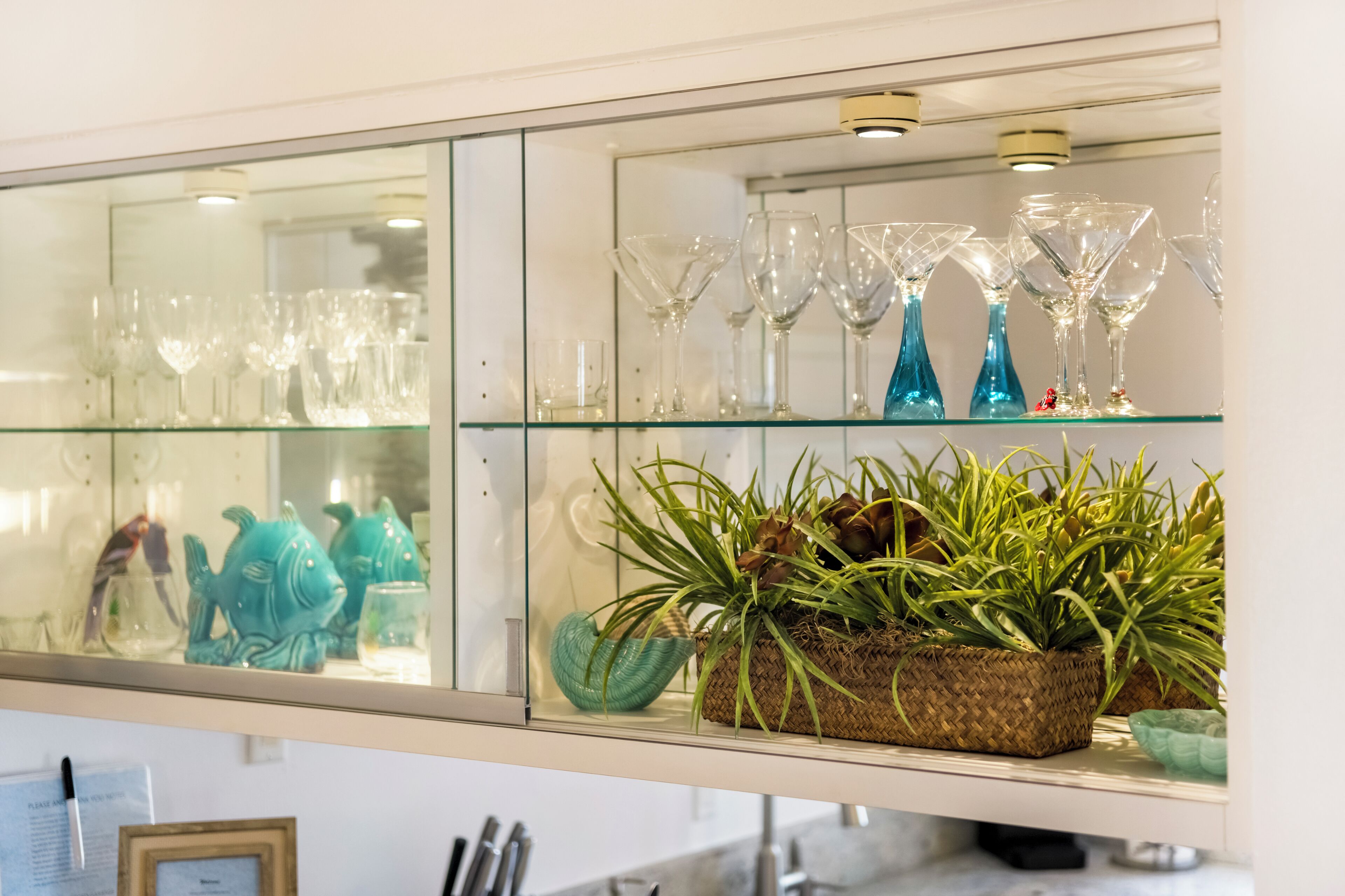 A glass display case with various glassware and a woven basket with green plants.