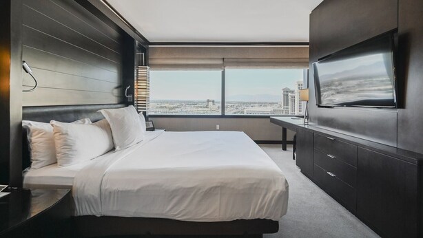 A modern hotel room with a large bed, a desk, and a TV on the wall.