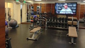 A gym with exercise equipment, a television screen, and a weight rack.