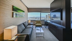 A modern hotel room with a large TV, a sofa, a desk, and a view of the cityscape.