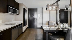 A modern kitchen with dark cabinets, a stainless steel microwave, a black door, and a dining area with a glass table and chairs.