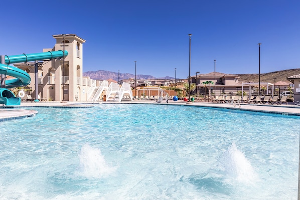 A swimming pool with a water slide, lounge chairs, and a view of mountains in the background.