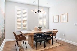A dining area with a wooden table, black chairs, a hanging light fixture, and a large window with blinds.