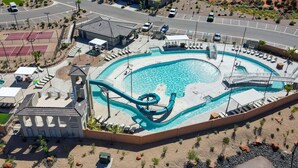 Una amplia piscina al aire libre con tobogán, rodeada de tumbonas y una cancha de tenis.