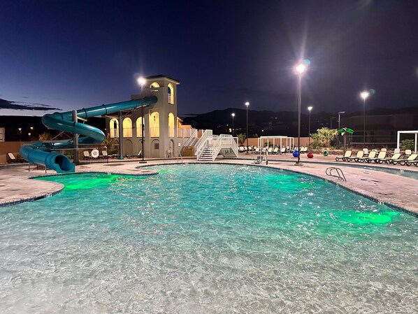 A swimming pool with a water slide, a tower, and lounge chairs.