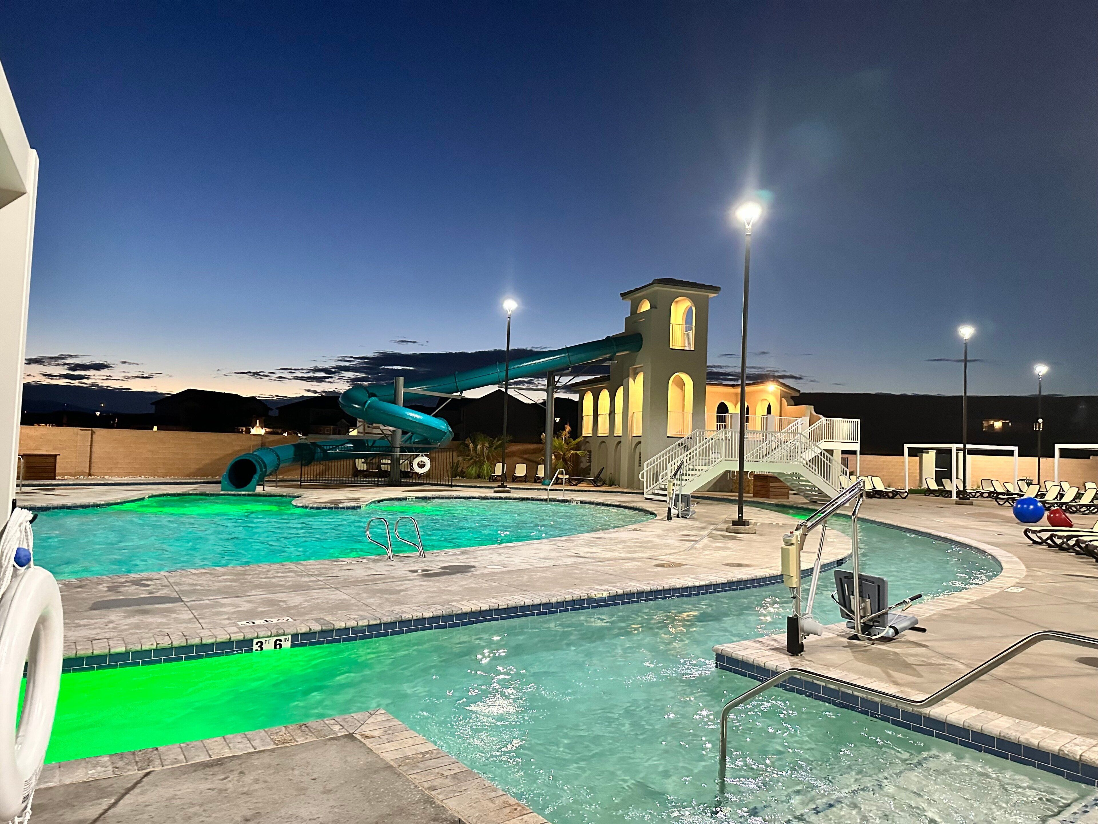 A swimming pool with a water slide, a staircase, and lounge chairs.