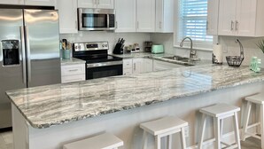 A modern kitchen with white cabinets, stainless steel appliances, a marble countertop, and pendant lighting. - Tupelo Bay Getaway. Stylish & Upscale Villa. Newly Built. Beach,Golf,Pools,Sun! (Murrells Inlet)
