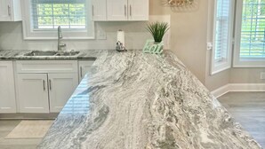 A kitchen with white cabinets, a marble island, and a pendant light. - Tupelo Bay Getaway. Stylish & Upscale Villa. Newly Built. Beach,Golf,Pools,Sun! (Murrells Inlet)