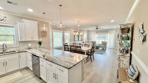 A spacious kitchen with white cabinets, a marble countertop, and a dining area with a table and chairs. - Tupelo Bay Getaway. Stylish & Upscale Villa. Newly Built. Beach,Golf,Pools,Sun! (Murrells Inlet)