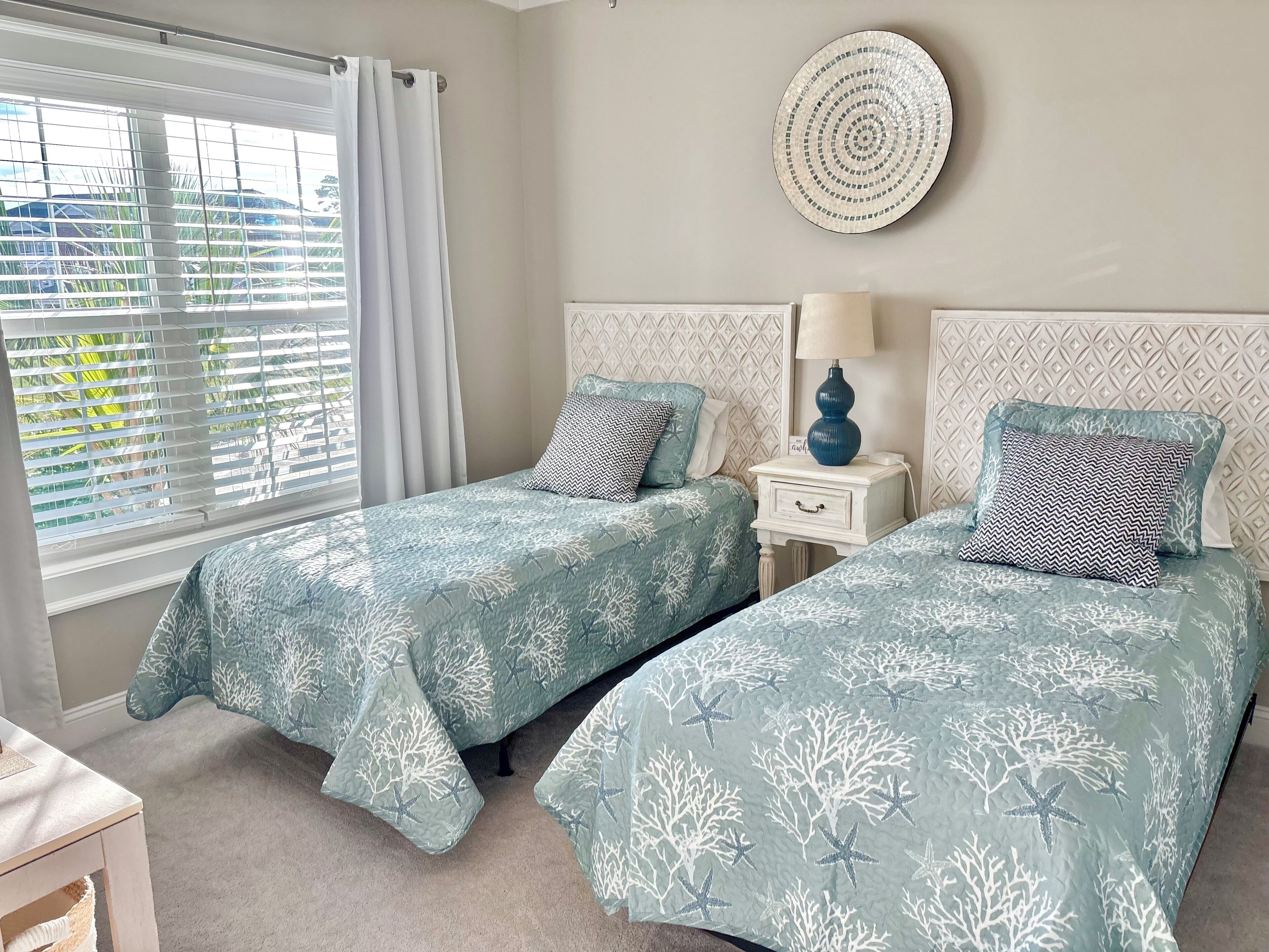 A bedroom with two beds, a bedside table with a lamp, and a decorative wall hanging.