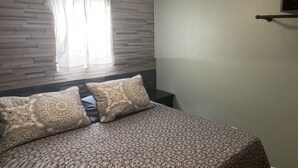 A bedroom with a bed, patterned bedding, a window with curtains, a wall-mounted light, and a small shelf. - Lakeview  pet friendly (Warsaw)