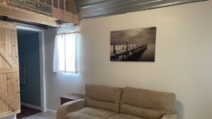 A beige sofa in a room with a wooden door, a small table, and a painting of a pier on the wall. - Lakeview  pet friendly (Warsaw)