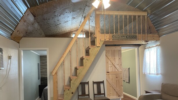 A loft bedroom with a wooden staircase, a loft bed, and a view of the living room. - Lakeview  pet friendly (Warsaw)