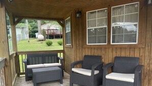 A covered porch with two wicker chairs and a bench, wooden railings, and a view of a backyard. - Lakeview  pet friendly (Warsaw)