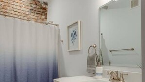 A bathroom with a white sink, a mirror, a toilet, and a shower curtain. - Majestic Lofts #201- Printers Alley Area (Nashville)