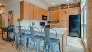 A modern kitchen with wooden cabinets, a black refrigerator, and a dining area with blue chairs. - Majestic Lofts #201- Printers Alley Area (Nashville)