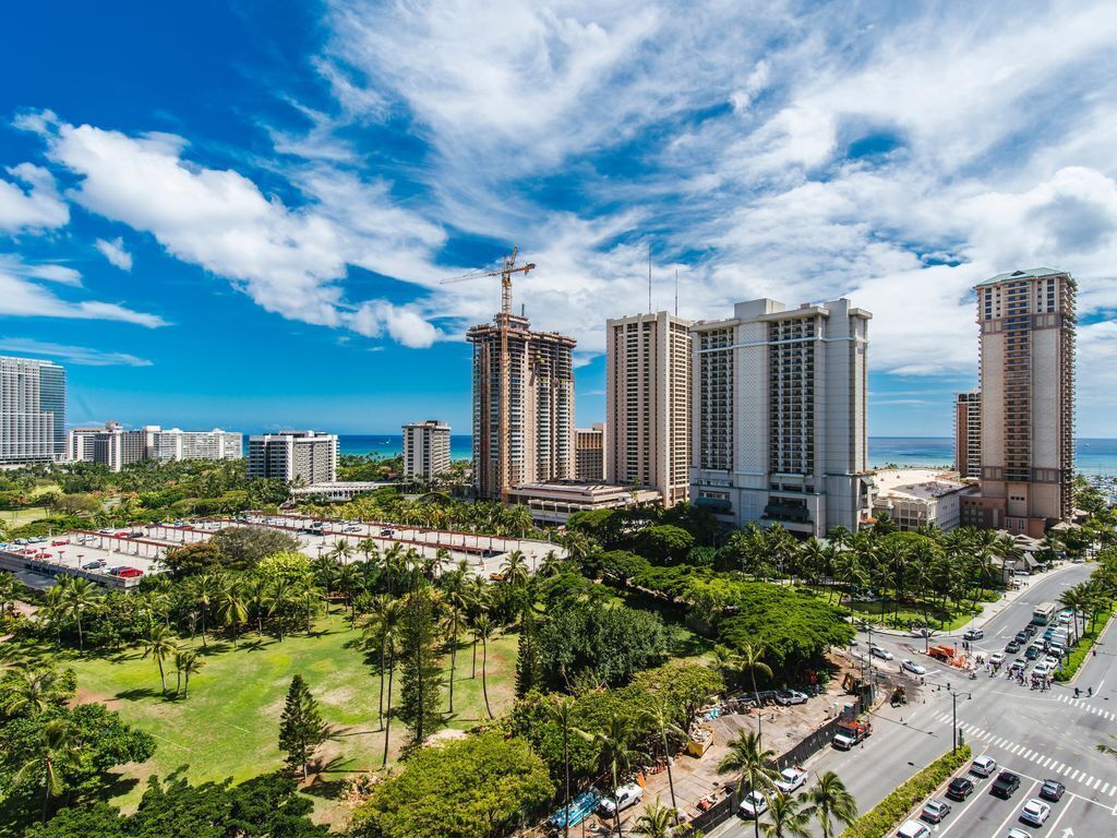 Un paisaje urbano con rascacielos, una grúa de construcción y vistas al mar.