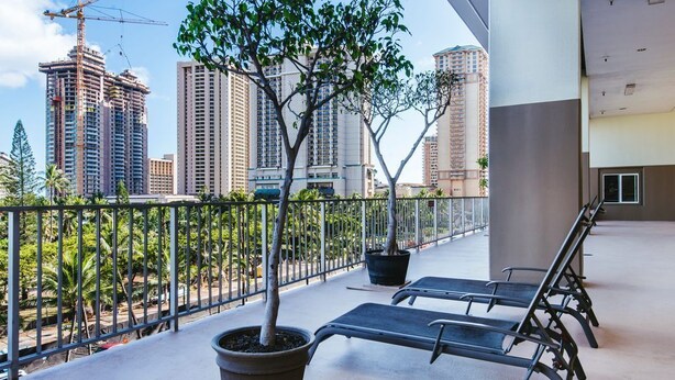 Un balcón con dos sillones de descanso y plantas en macetas, con vista a un paisaje urbano con edificios altos y grúas de construcción.