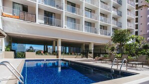 Una piscina con agua cristalina azul, rodeada por un edificio blanco con balcones.