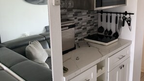 Una kitchenette compacta con microondas, estufa y utensilios colgantes.