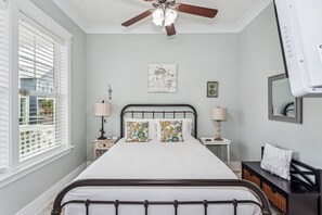 A bedroom with a bed, two bedside tables with lamps, a ceiling fan, a window with blinds, and a wall-mounted mirror. - Seaside Cottage: Community Pool, Hot Tub and Gated. Sleeps 11. Dog Friendly! (Navarre)