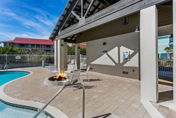 Uma área de piscina ao ar livre coberta, com espreguiçadeiras, lareira e vista da piscina para um edifício com telhado vermelho.