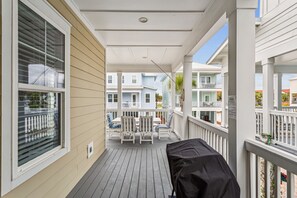 A covered porch with a grill, white railings, and a view of neighboring buildings. - Seaside Cottage: Community Pool, Hot Tub and Gated. Sleeps 11. Dog Friendly! (Navarre)