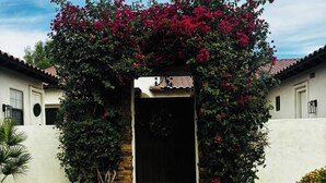 A building entrance with a brick pathway leading to a black door, surrounded by a flowering archway. - Private Casita w/ New Full Kitchen, Private Pool, Gated Community (Goodyear)