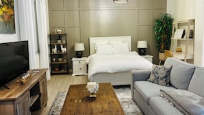 A modern bedroom with a bed, bedside tables, a TV, a coffee table with flowers, a sofa, and a plant. - Private Casita w/ New Full Kitchen, Private Pool, Gated Community (Goodyear)