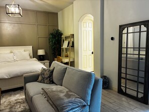 A bedroom with a bed, a sofa, a desk, a plant, and a door with a window view.